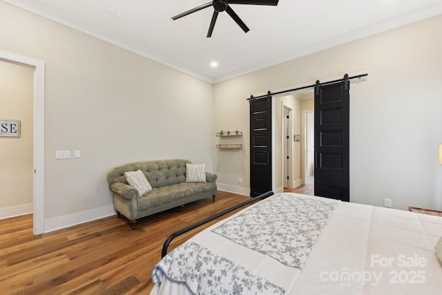 bedroom featuring ceiling fan, a barn door, wood-type flooring, and ornamental molding