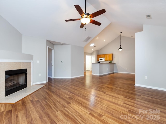 unfurnished living room with a tile fireplace, ceiling fan, light hardwood / wood-style flooring, and vaulted ceiling