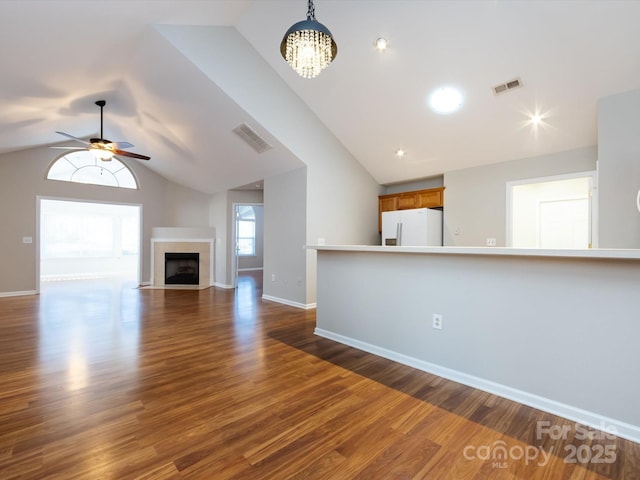 unfurnished living room with ceiling fan with notable chandelier, dark hardwood / wood-style flooring, and vaulted ceiling