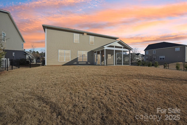 back house at dusk featuring a sunroom and a lawn