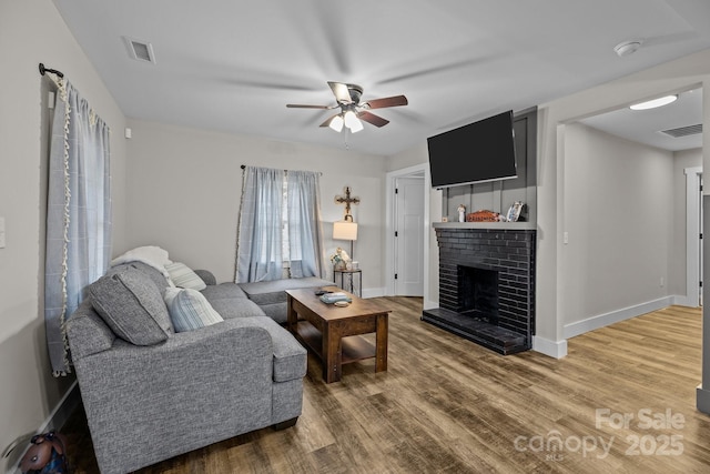 living room featuring ceiling fan, wood-type flooring, and a brick fireplace