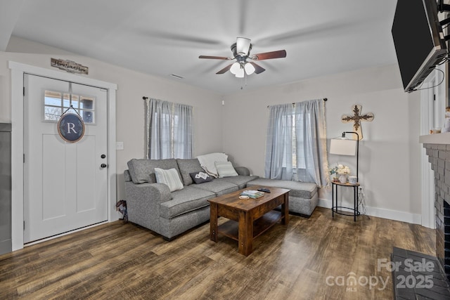 living room featuring ceiling fan, a fireplace, and dark wood-type flooring