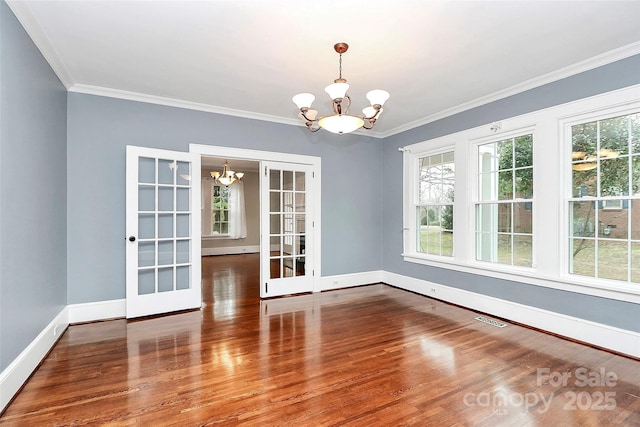 unfurnished dining area featuring hardwood / wood-style flooring, ornamental molding, french doors, and an inviting chandelier