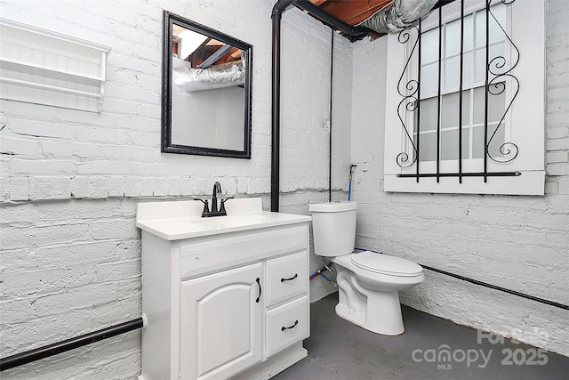 bathroom with vanity, concrete flooring, brick wall, and toilet