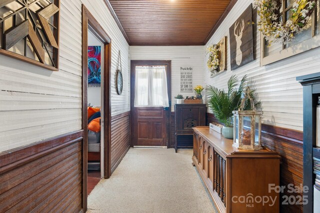 entryway with wood walls, light colored carpet, and wood ceiling