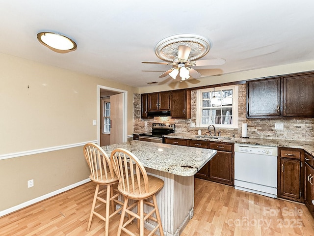 kitchen with a breakfast bar, sink, dishwasher, a center island, and stainless steel range with electric cooktop