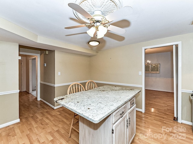 kitchen with a breakfast bar, ceiling fan, a kitchen island, and light wood-type flooring