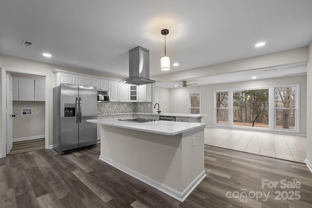 kitchen featuring backsplash, white cabinets, appliances with stainless steel finishes, island range hood, and kitchen peninsula