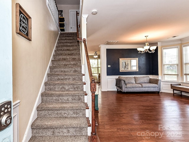 stairs with crown molding, wood-type flooring, and a notable chandelier