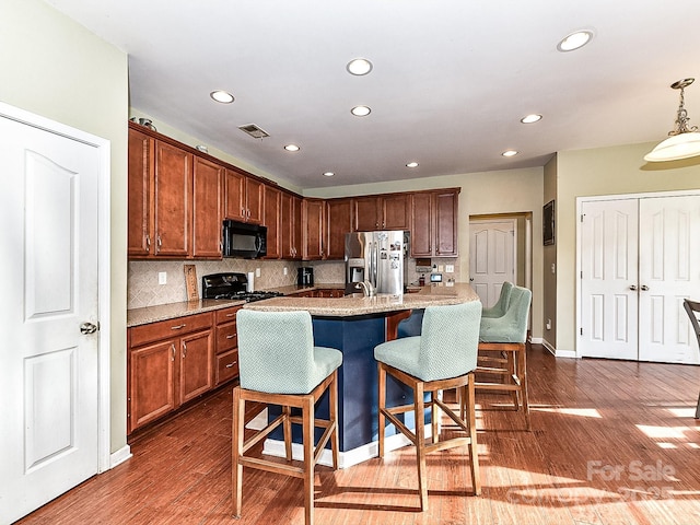 kitchen with backsplash, dark wood-type flooring, black appliances, hanging light fixtures, and an island with sink