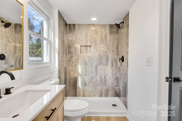 bathroom featuring tiled shower, vanity, toilet, and a wealth of natural light