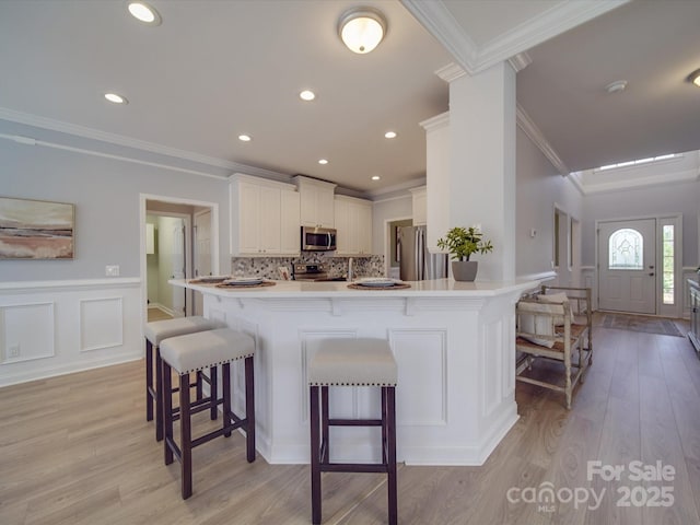 kitchen featuring white cabinets, crown molding, appliances with stainless steel finishes, a kitchen bar, and kitchen peninsula