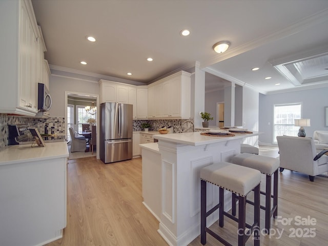 kitchen with kitchen peninsula, tasteful backsplash, ornamental molding, stainless steel appliances, and white cabinetry