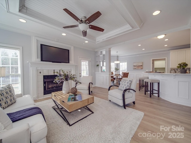 living room featuring a tile fireplace, light hardwood / wood-style floors, a raised ceiling, and crown molding