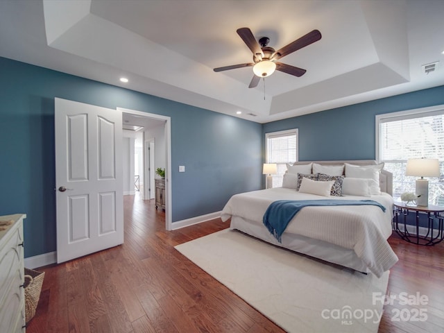 bedroom featuring ceiling fan, dark wood-type flooring, and a tray ceiling