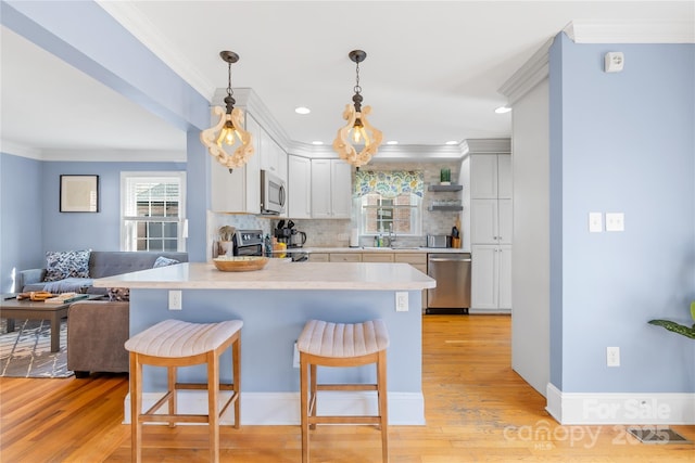 kitchen with appliances with stainless steel finishes, hanging light fixtures, a kitchen breakfast bar, tasteful backsplash, and white cabinets