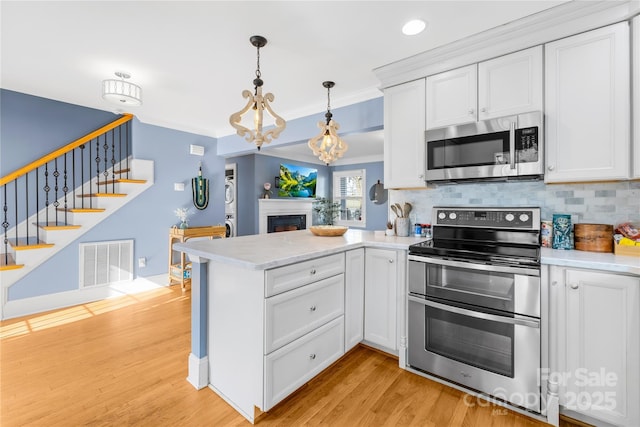 kitchen featuring appliances with stainless steel finishes, white cabinets, backsplash, and decorative light fixtures