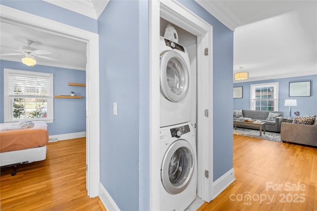 clothes washing area with crown molding, ceiling fan, stacked washer / drying machine, and light wood-type flooring