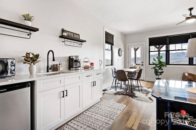 kitchen with white cabinets, ceiling fan, sink, dishwasher, and light hardwood / wood-style floors