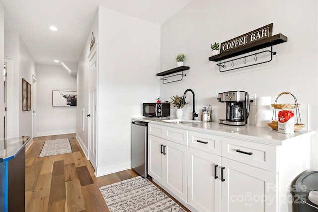 bar with light hardwood / wood-style floors, white cabinetry, sink, and fridge