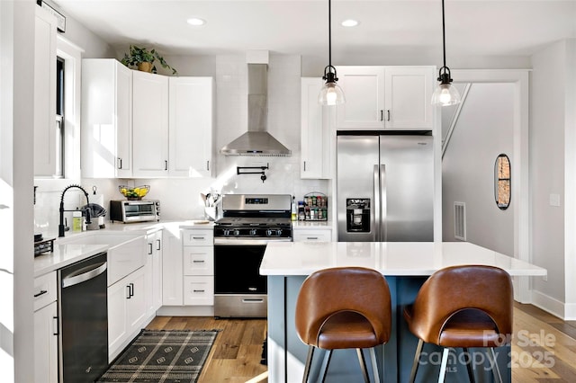 kitchen with a center island, white cabinets, wall chimney range hood, hanging light fixtures, and appliances with stainless steel finishes