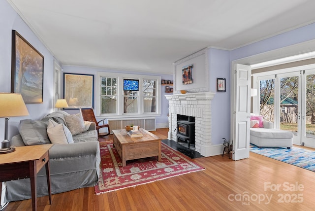 living room featuring wood-type flooring, radiator heating unit, crown molding, and a wood stove