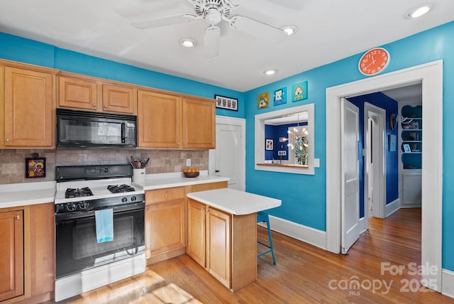 kitchen featuring a kitchen bar, backsplash, ceiling fan with notable chandelier, light hardwood / wood-style floors, and range with gas stovetop