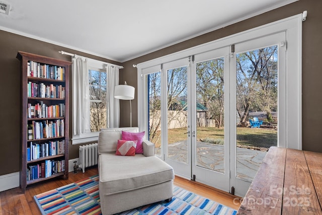 living area with radiator heating unit, dark hardwood / wood-style flooring, and ornamental molding