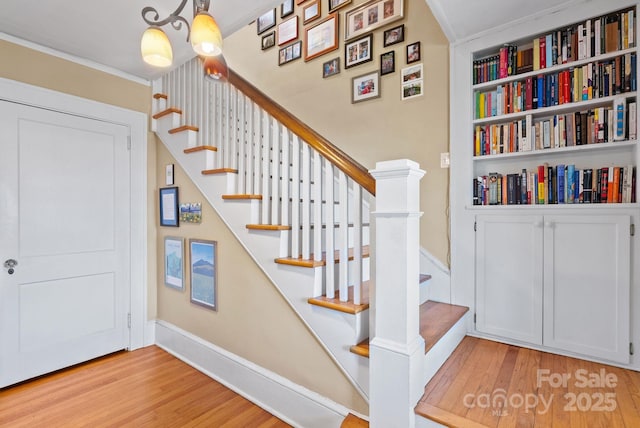 staircase with built in shelves, ornamental molding, and hardwood / wood-style floors