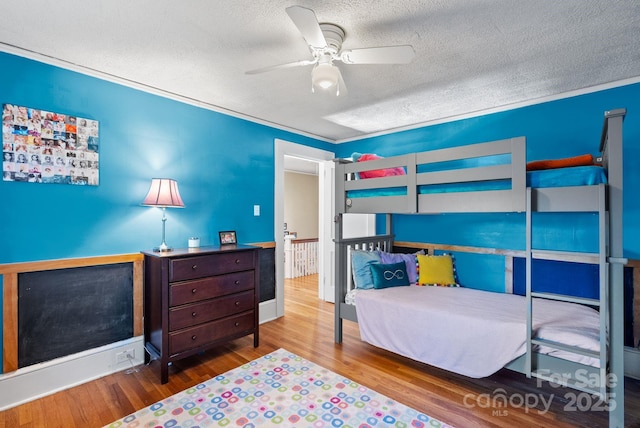 bedroom with ceiling fan, wood-type flooring, a textured ceiling, and ornamental molding