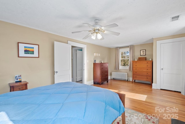 bedroom with ceiling fan, light wood-type flooring, radiator heating unit, and a textured ceiling