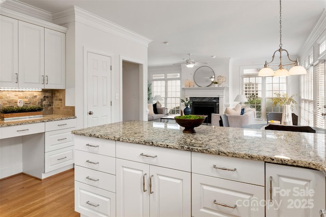 kitchen featuring crown molding, a premium fireplace, white cabinetry, tasteful backsplash, and decorative light fixtures