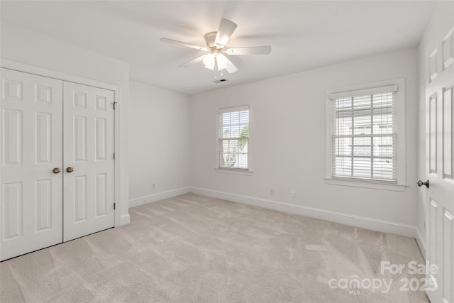 unfurnished bedroom with ceiling fan, light carpet, and a closet