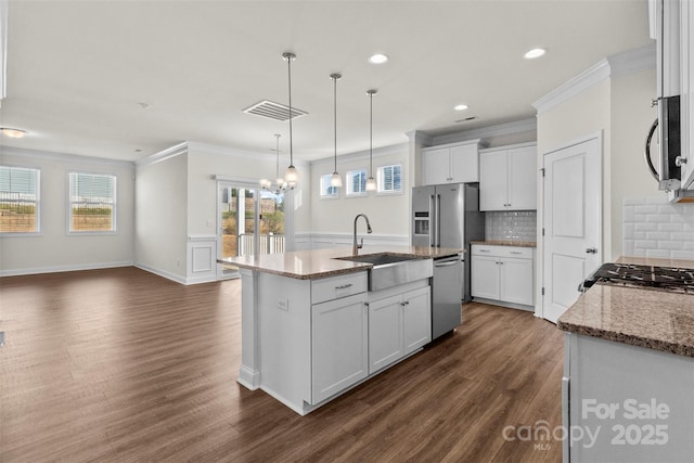 kitchen with a center island with sink, hanging light fixtures, sink, appliances with stainless steel finishes, and white cabinetry