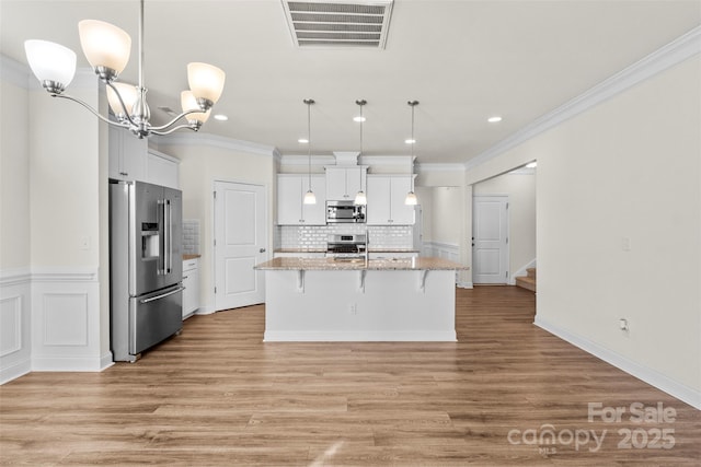 kitchen featuring white cabinets, decorative light fixtures, a center island with sink, and stainless steel appliances