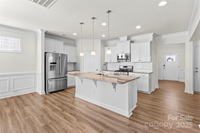 kitchen with appliances with stainless steel finishes, light stone counters, a center island with sink, white cabinetry, and a breakfast bar area