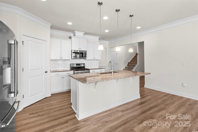 kitchen featuring stainless steel appliances, sink, pendant lighting, white cabinetry, and an island with sink