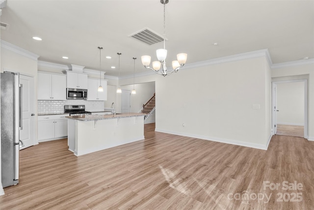 kitchen with a kitchen bar, stainless steel appliances, a kitchen island with sink, pendant lighting, and white cabinets