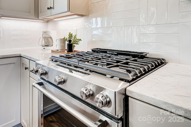 details with stainless steel gas stove, decorative backsplash, light stone countertops, and gray cabinetry