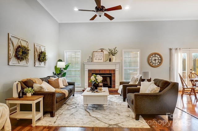 living room featuring a fireplace, a high ceiling, ceiling fan, light wood-type flooring, and french doors