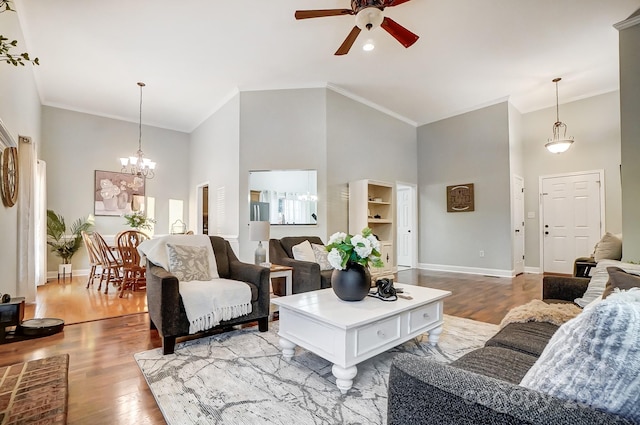 living room with a high ceiling, crown molding, ceiling fan with notable chandelier, and light hardwood / wood-style flooring