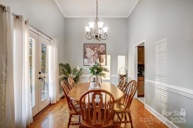 dining area featuring crown molding, a notable chandelier, light hardwood / wood-style floors, and french doors