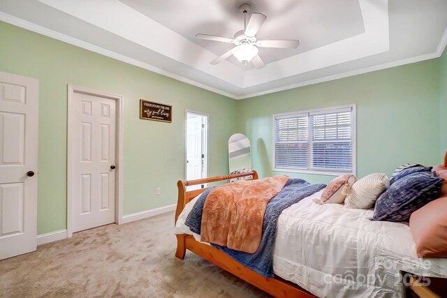 bedroom with ceiling fan, ornamental molding, a raised ceiling, and light colored carpet