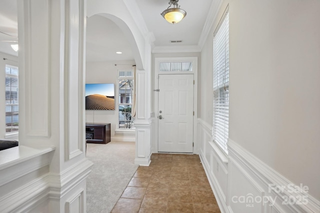 interior space with a decorative wall, light colored carpet, arched walkways, and a wealth of natural light