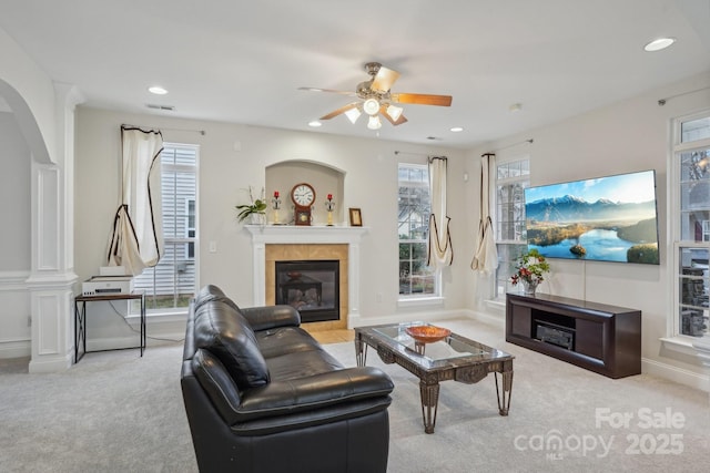 living area featuring a ceiling fan, visible vents, arched walkways, a tile fireplace, and carpet flooring