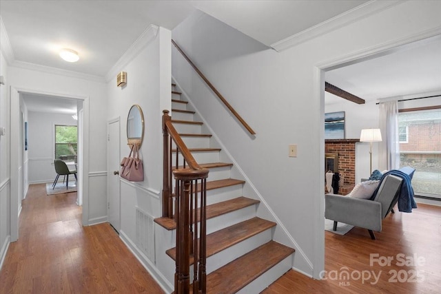 staircase with a brick fireplace, ornamental molding, and hardwood / wood-style floors