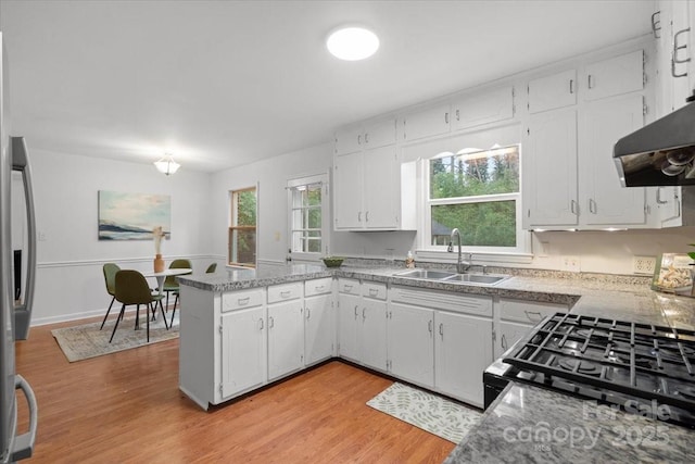 kitchen with white cabinets, stainless steel refrigerator with ice dispenser, light hardwood / wood-style floors, sink, and kitchen peninsula