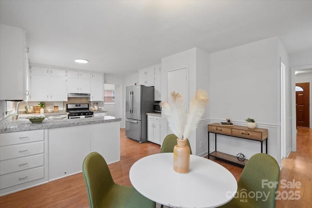 kitchen featuring light wood-type flooring, kitchen peninsula, stainless steel appliances, and white cabinets