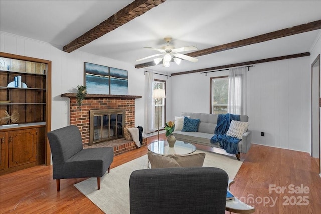 living room with light wood-type flooring, a brick fireplace, beam ceiling, and ceiling fan