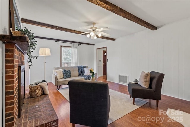 living room featuring hardwood / wood-style flooring, beam ceiling, ceiling fan, and a fireplace